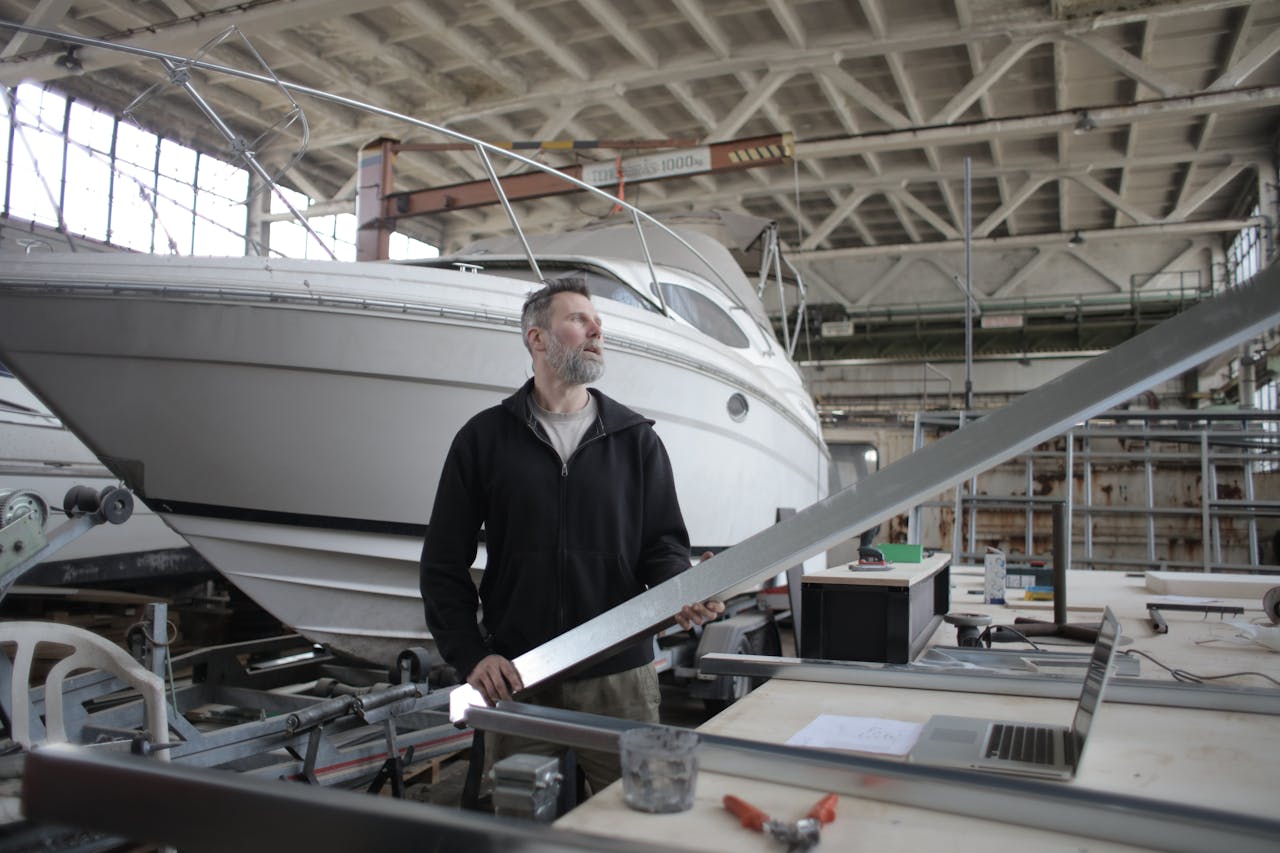 client-satisfaction-img Side view of adult bearded workman in casual clothes standing near workbench and controlling metal detail in garage with yachts